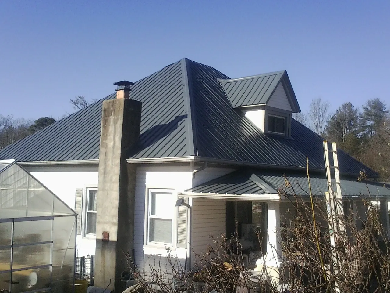 Dark blue standing seam metal roof on a white farmhouse with dormer — Slate & Tile Roof Repair by Roofing Brothers in Gazelle