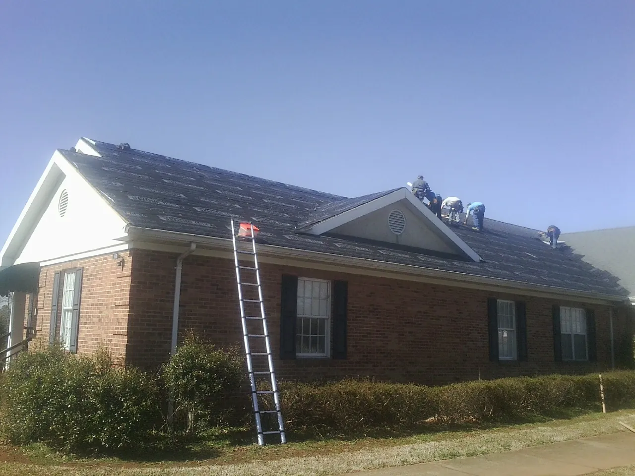 Crew tearing shingles off a brick ranch roof with a ladder set — Emergency Roof Repair work by our crew in Gazelle