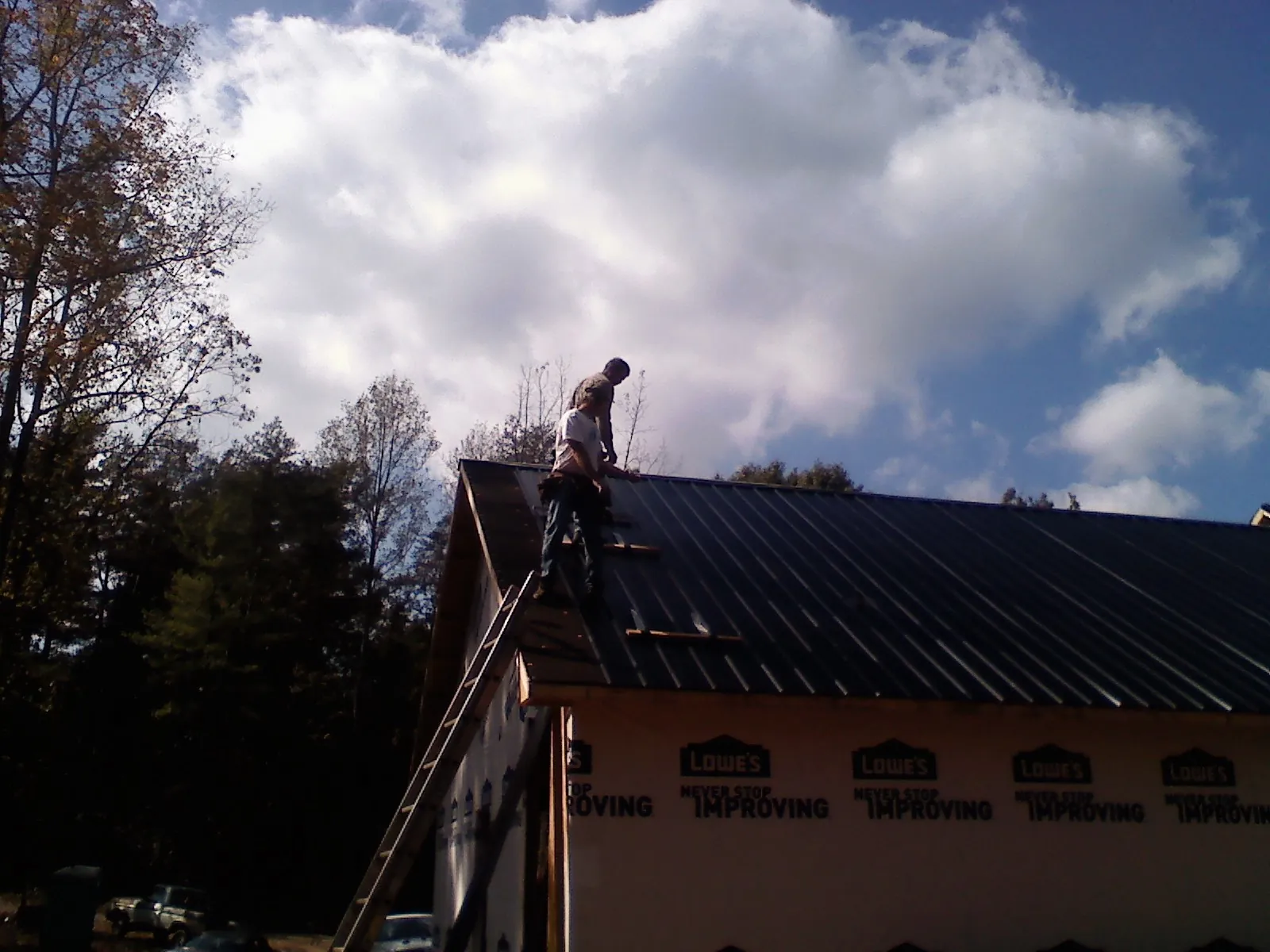 Roofer fastening dark metal panels high against a cloudy sky, from a Roof Inspection job in Gazelle