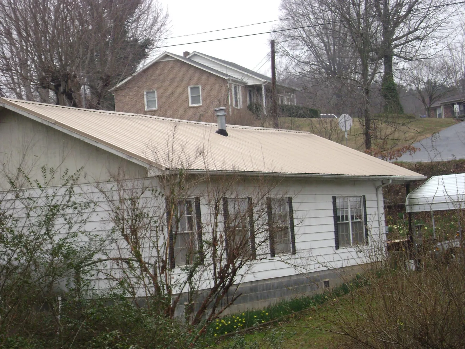 Tan metal roof on a white sided house set into a hillside — Commercial Roofing by Roofing Brothers in Gazelle